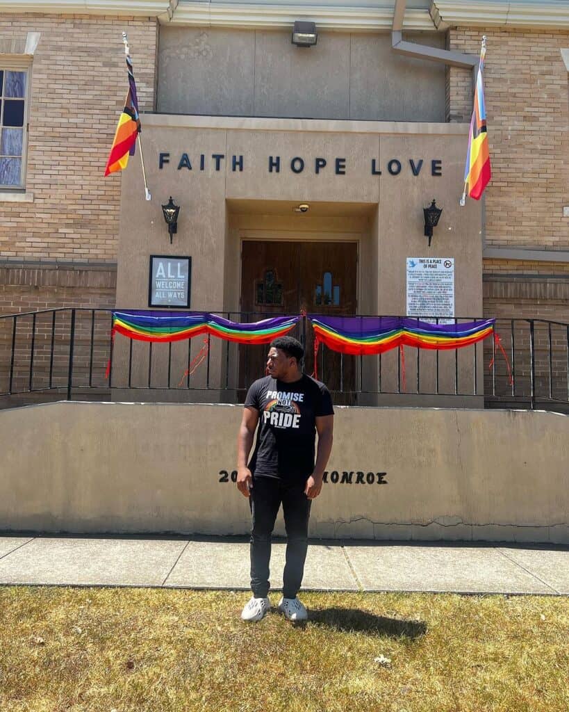 Bryson Gray in front of church with rainbow flag and a promise not pride t-shirt (faith)